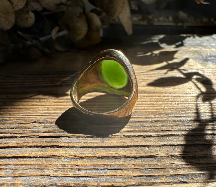 Gold ring featuring three green jade beads across the top on a wooden surface