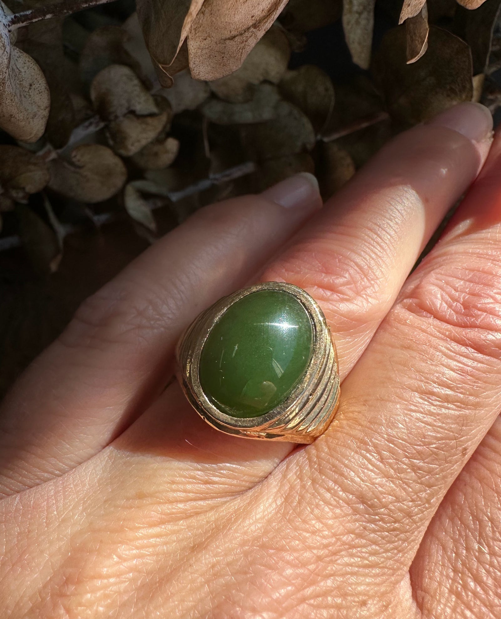 Oval green jade cabochon set in a textured gold ring worn on the finger
