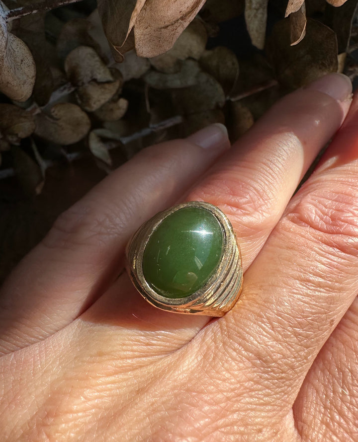Oval green jade cabochon set in a textured gold ring worn on the finger