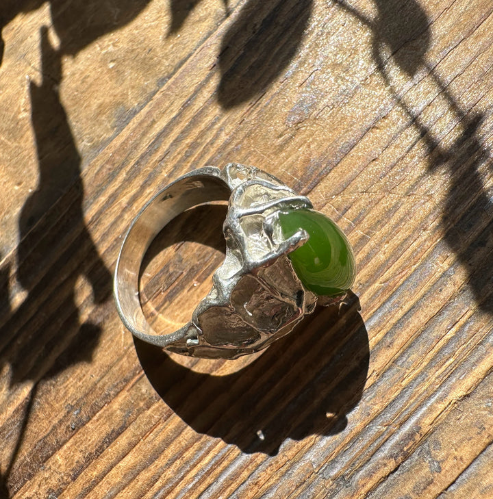 Top view of Jade Hammered Ring featuring a green jade cabochon in a rugged silver setting on a wooden surface.