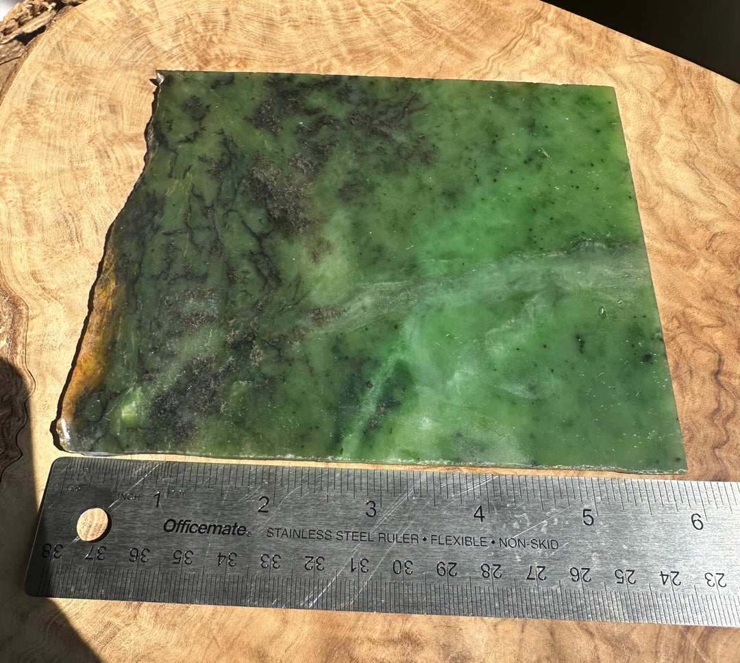 A rectangular green stone slab with natural marbling and rough edges, placed on a wooden surface with a metal ruler below it for scale.