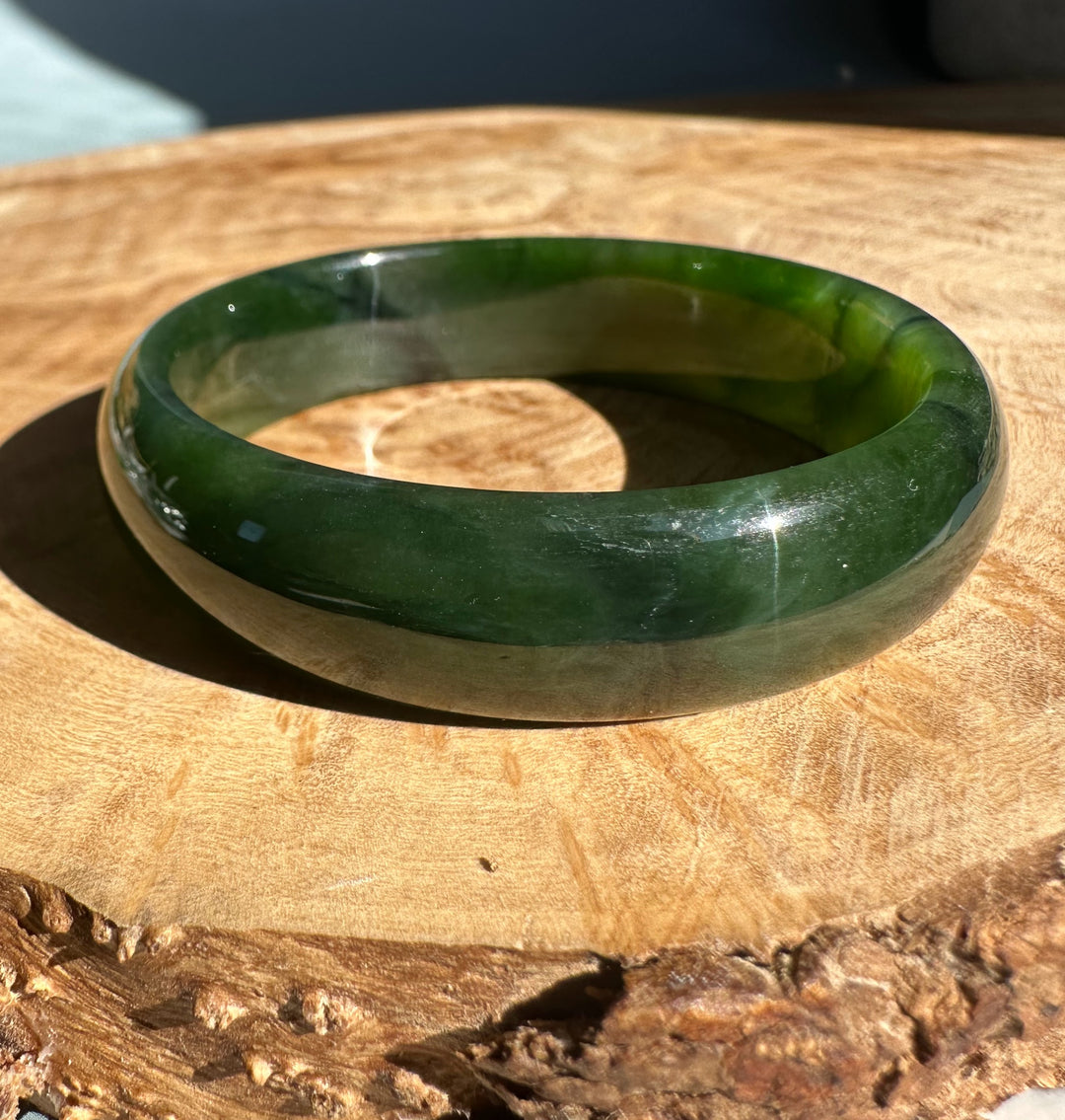 Rich green Canadian nephrite jade bangle resting on a wooden surface