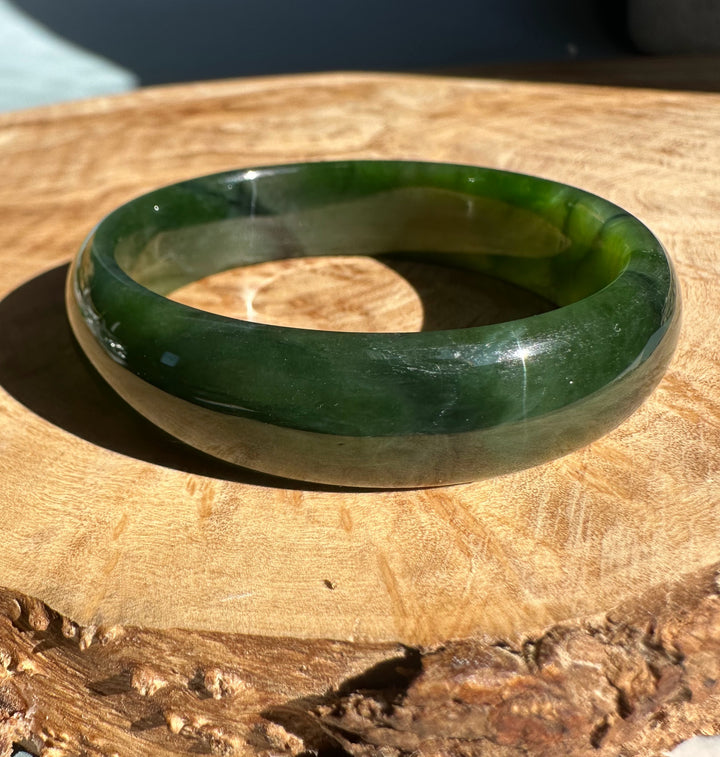 Rich green Canadian nephrite jade bangle resting on a wooden surface