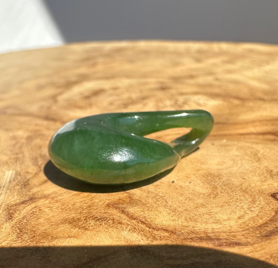 A polished green jade pendant stone ornament resting on a textured wooden surface.