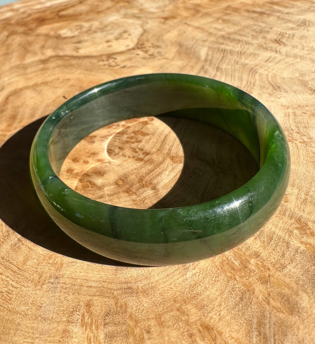 Side angle of rich green nephrite jade bangle on wood showing thickness and polished banding