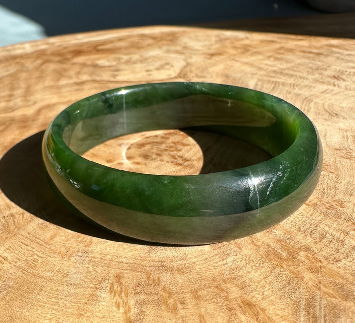 Rich green Canadian nephrite jade bangle with a smooth polished surface resting on a wood table