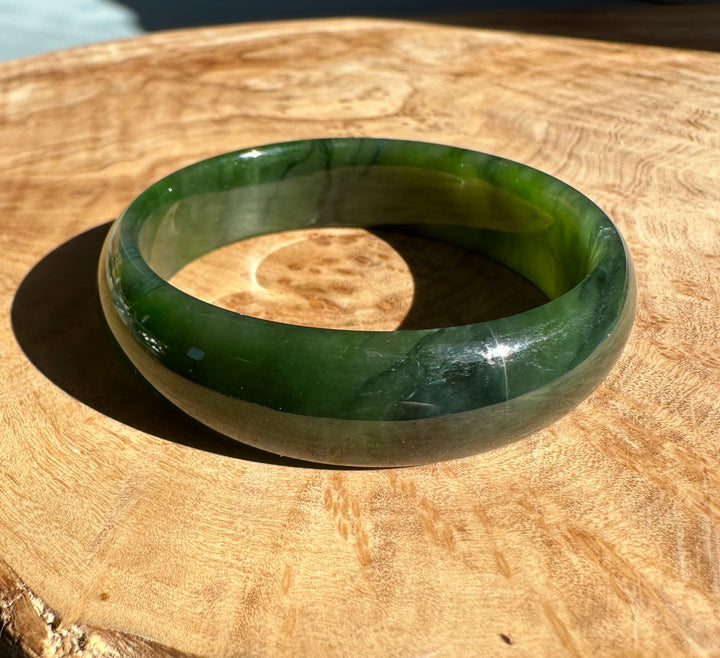 Translucent green nephrite jade bangle catching sunlight on a wooden surface.