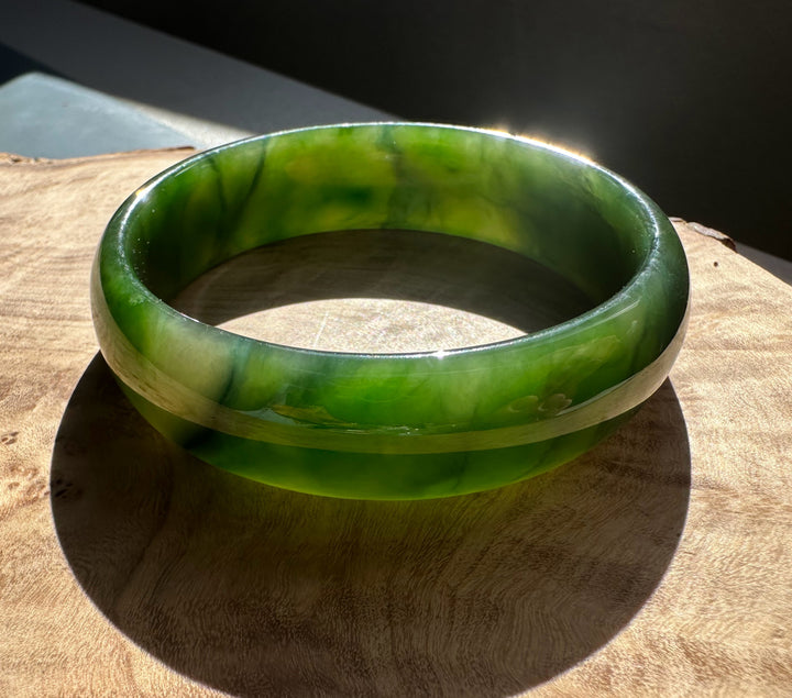 Rich green Canadian nephrite jade bangle resting on a wooden surface