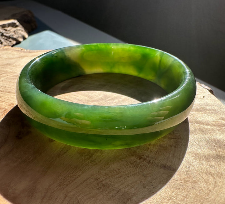 Rich green Canadian nephrite jade bangle with a glossy finish resting on a wooden surface.