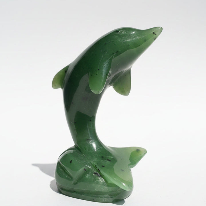 A polished green jade dolphin figurine standing on a wooden surface against a neutral light background.