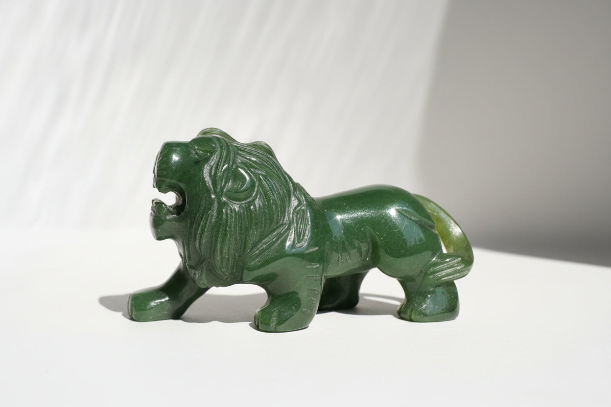 A small carved green jade lion figurine with an open mouth, standing on a light background.