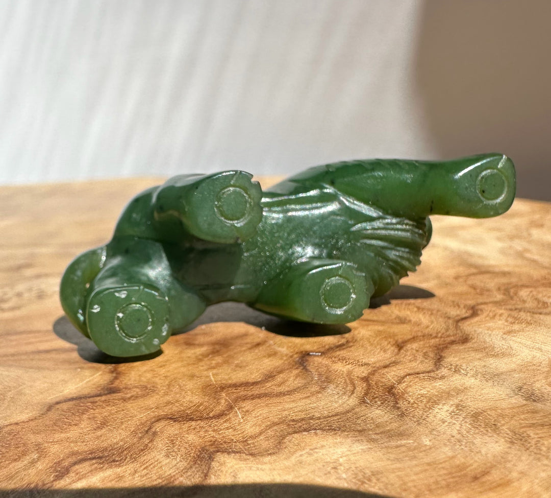 A small carved green jade lions feet, resting on a polished wood surface with a neutral background.