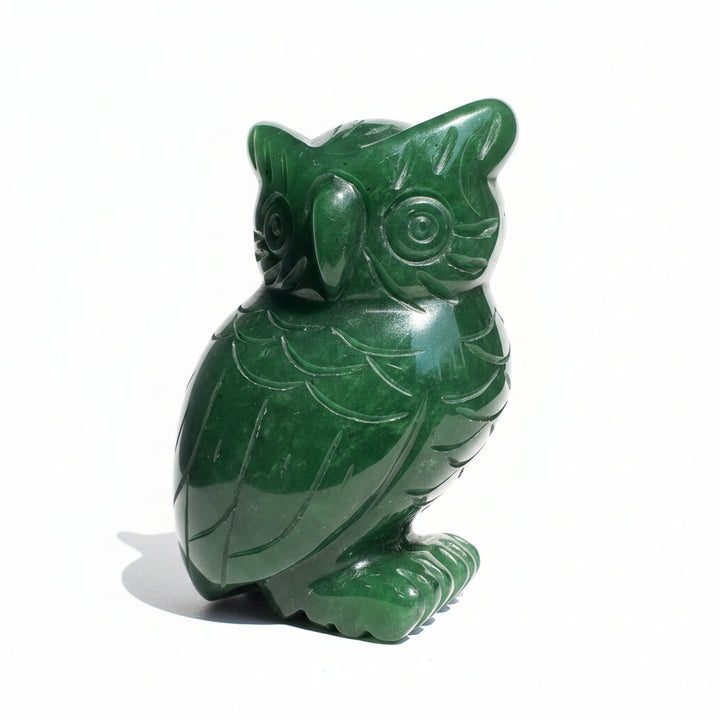 A carved green jade owl figurine sitting on a white surface background.