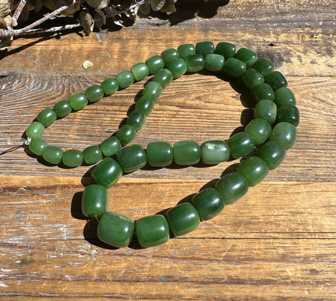 Siberian Jade barrel beads arranged on a wooden surface in a loose unstrung strand