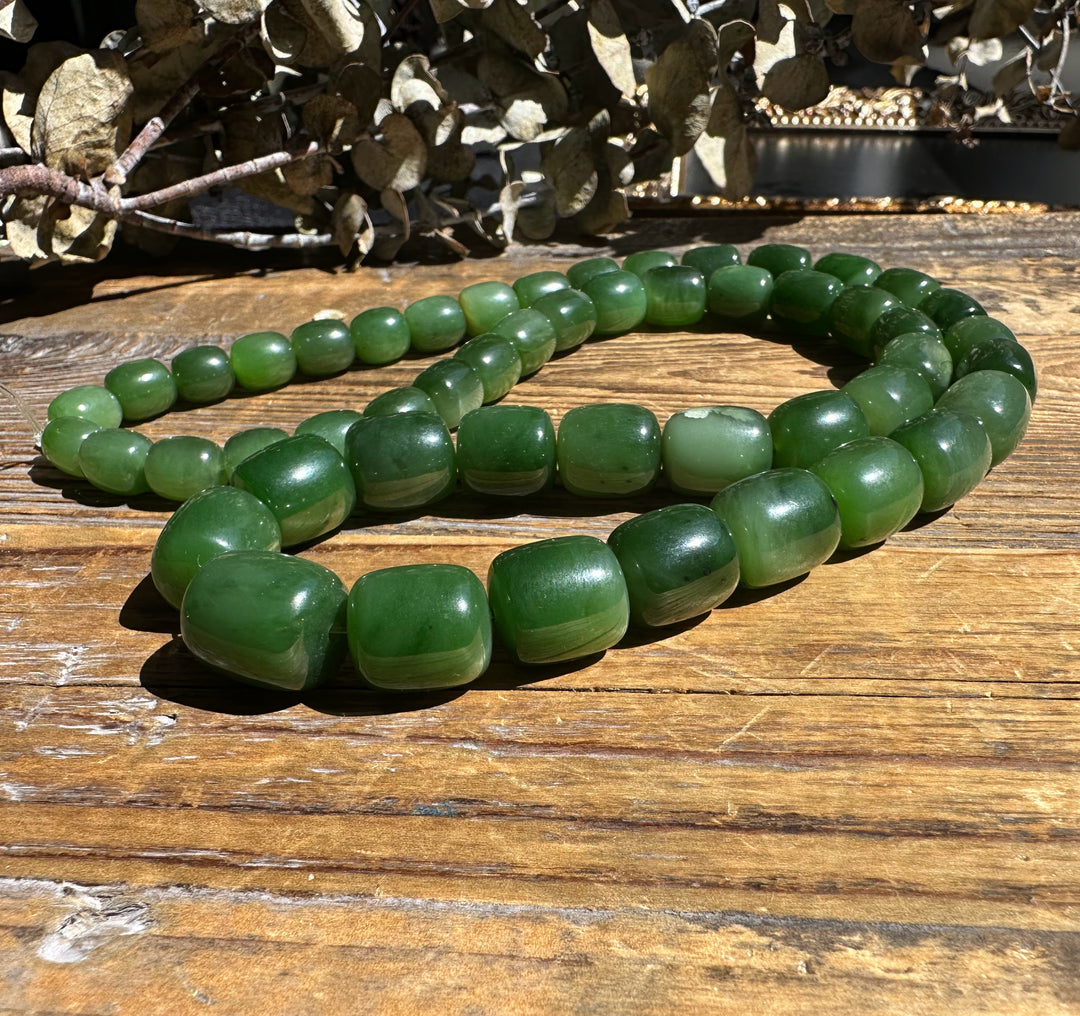Siberian Jade barrel beads on an unstrung graduated strand coiled on wood