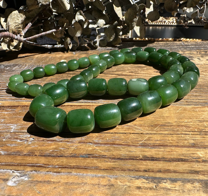 Siberian Jade barrel beads on an unstrung graduated strand coiled on wood
