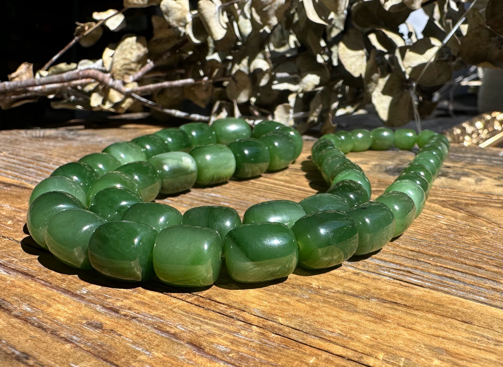 Close-up of green Siberian jade barrel beads on a wooden surface, unstrung and spaced along a strand.