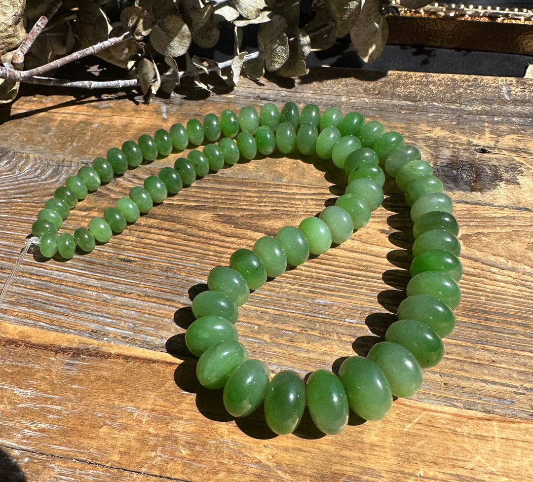 Green jade Siberian Abacus beads in an 18 inch unstrung strand laid on a rustic wooden surface