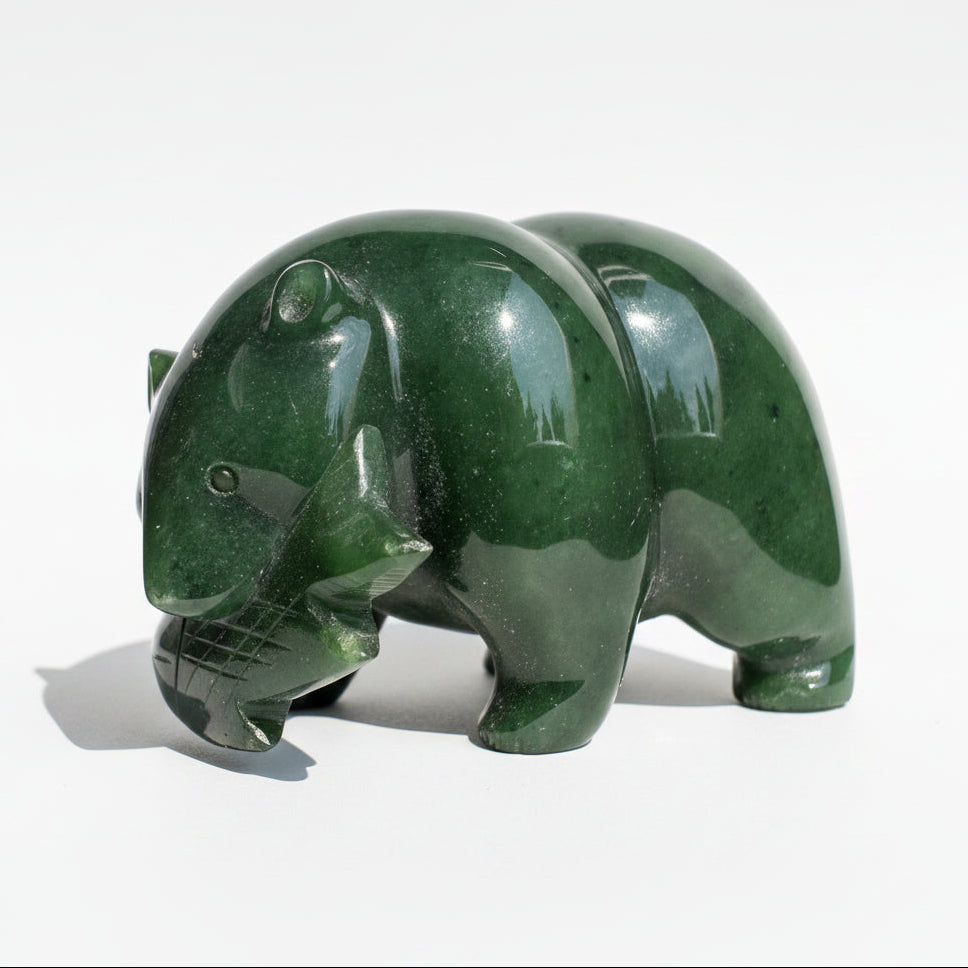 A polished dark green jade sculpture of a bear standing on a white background.