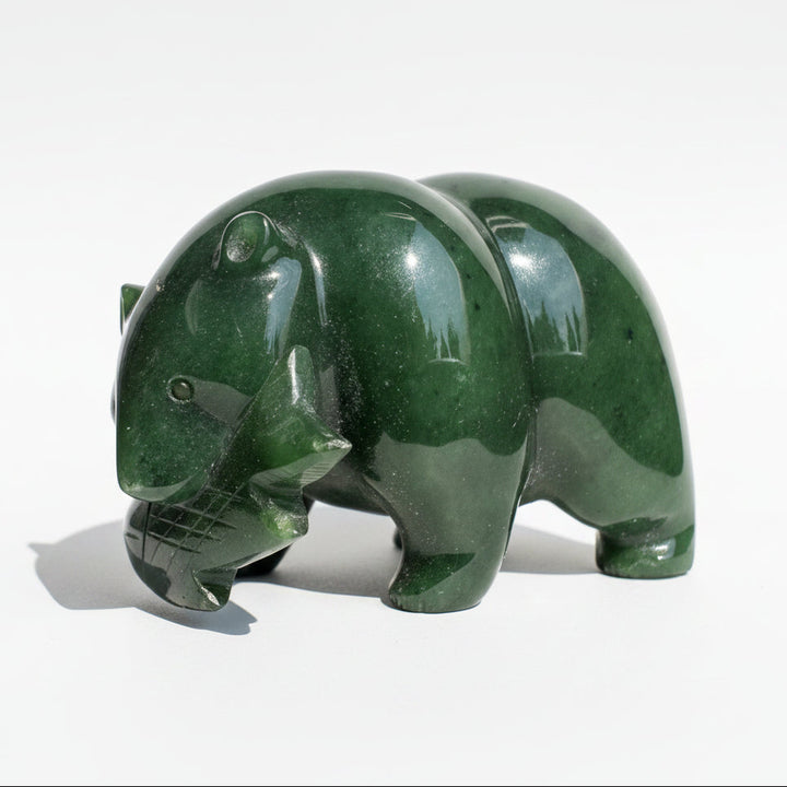 A polished dark green jade sculpture of a bear standing on a white background.