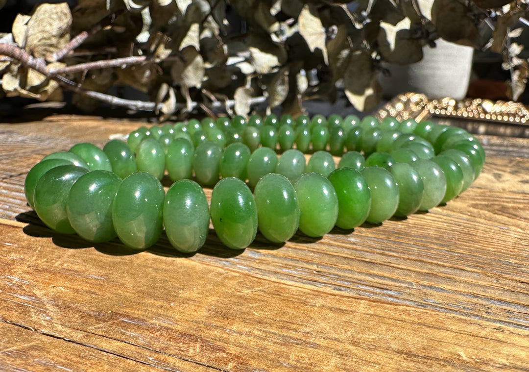 Close up of green Siberian Abacus beads on an 18 inch unstrung strand coiled on a wooden table