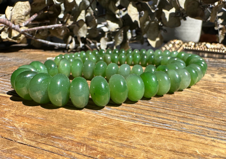 Close up of green Siberian Abacus beads on an 18 inch unstrung strand coiled on a wooden table