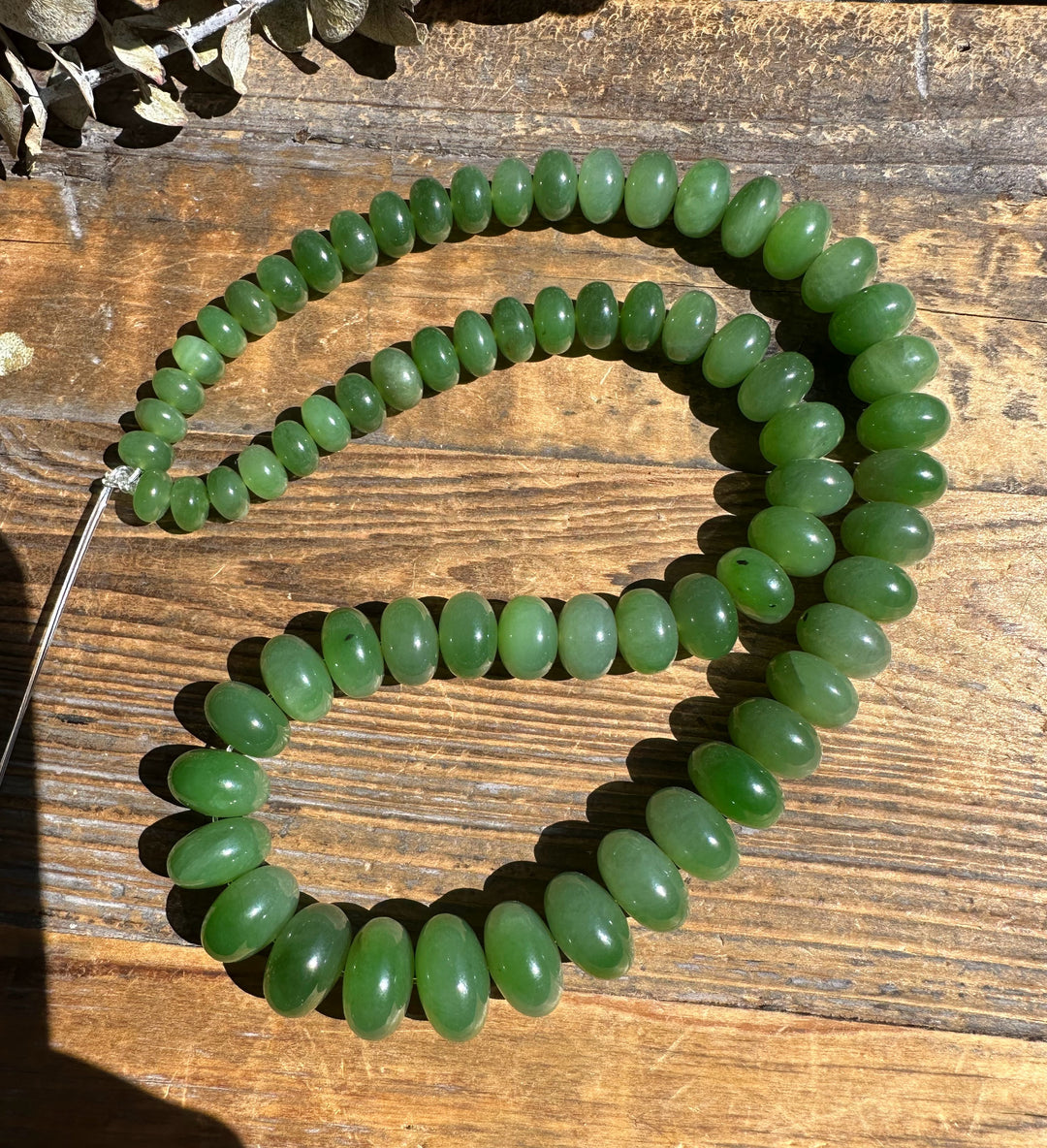 Green oval Siberian Abacus beads on a wooden surface forming a long unstrung 18 inch strand