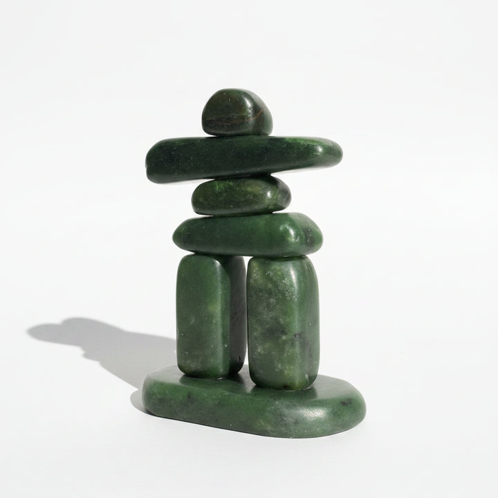 A green jade inukshuk sculpture standing on a neutral white  background.
