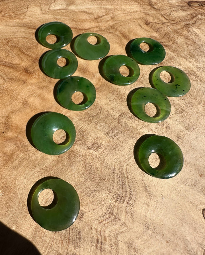 Collection of green jade donut pendants arranged on a textured wooden surface