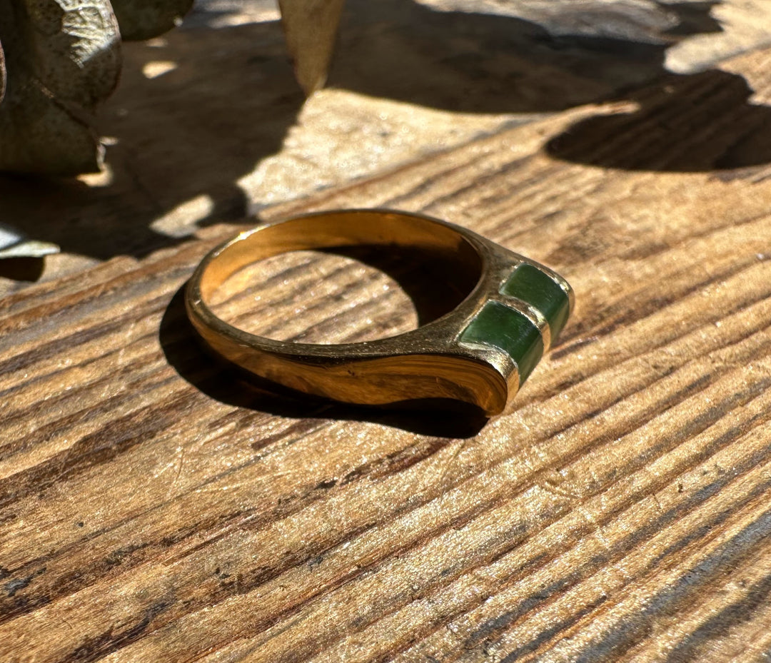 Gold band ring with two green jade insets on a sunlit wooden surface.