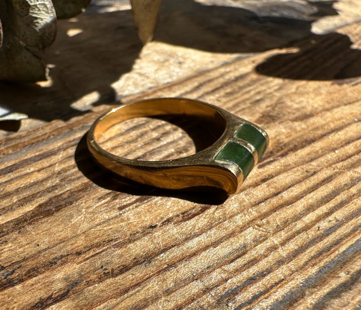 Gold band ring with two green jade insets on a sunlit wooden surface.
