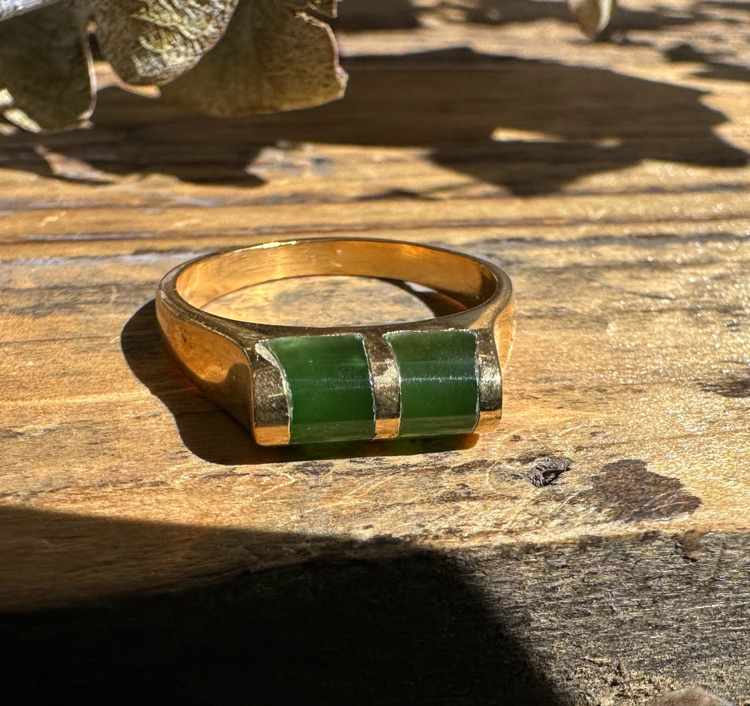Close up of vintage jade ring showing two green stones set in gold on a textured wooden surface.