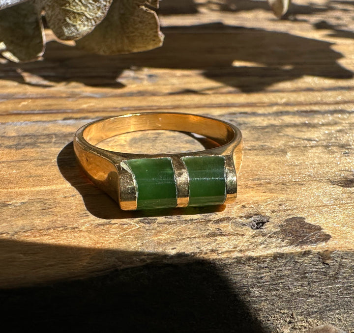 Close up of vintage jade ring showing two green stones set in gold on a textured wooden surface.