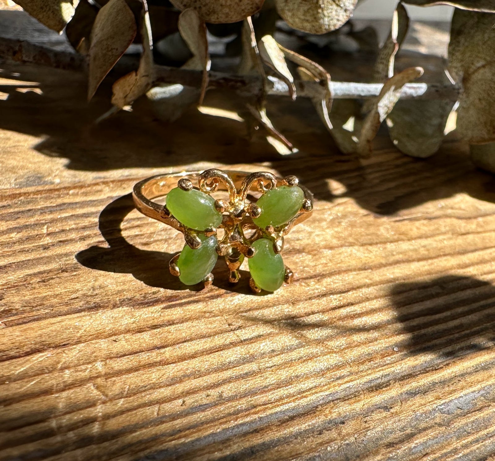 Close up of Vintage Jade Butterfly Ring showing green jade stones and gold butterfly setting on a wooden surface