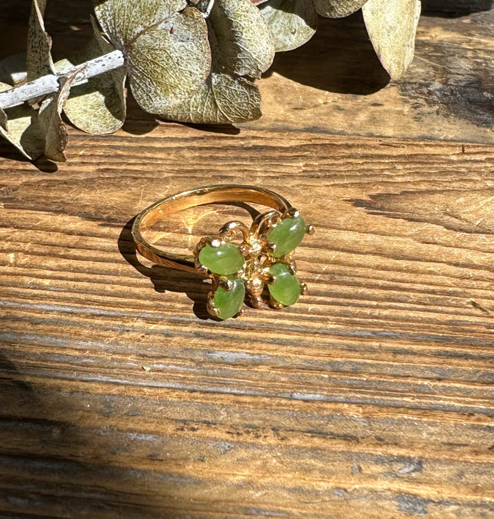 Gold vintage butterfly ring with four green jade stones on a rustic wooden surface