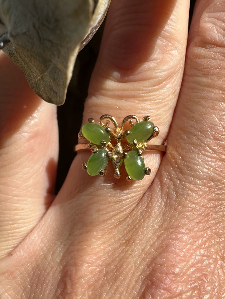 Close up of a jade butterfly ring worn on a finger with four green stones set in gold