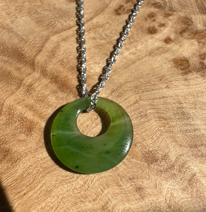 Donut shaped green jade pendant with a central hole on a silver chain