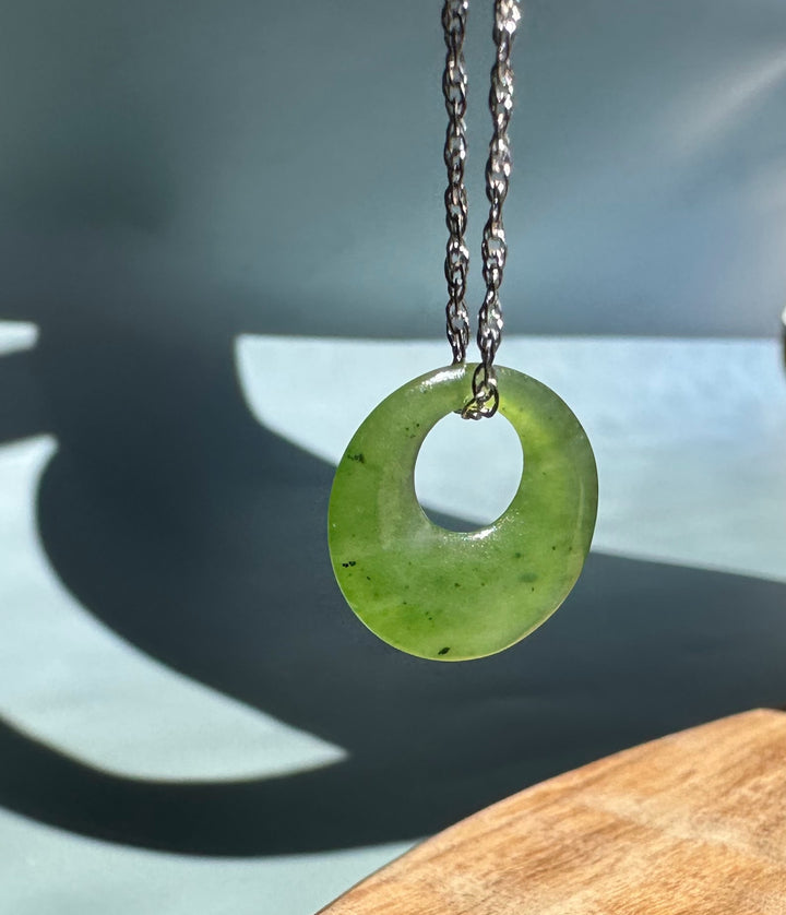 Circular jade pendant with central hole suspended on a silver chain