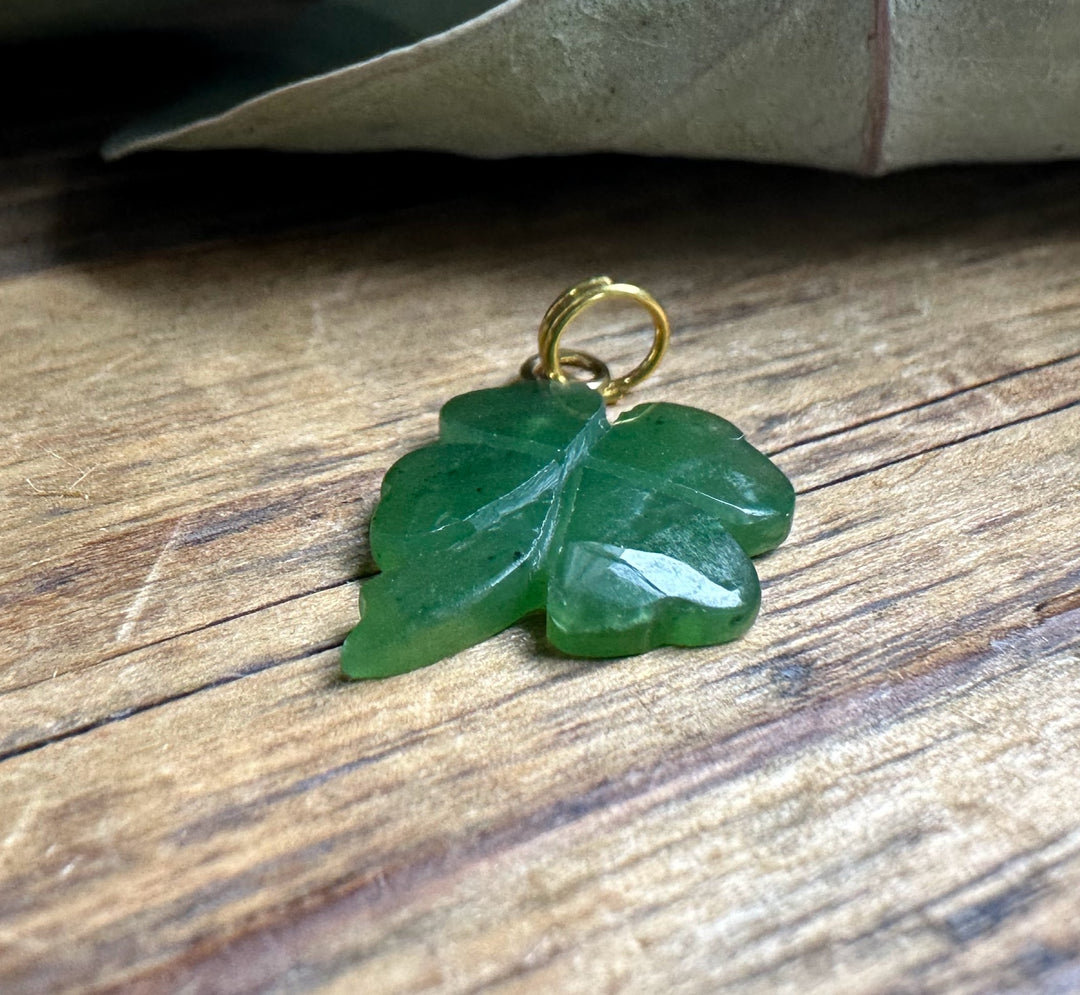 Close-up of green shamrock charm with a gold loop on a wood background.