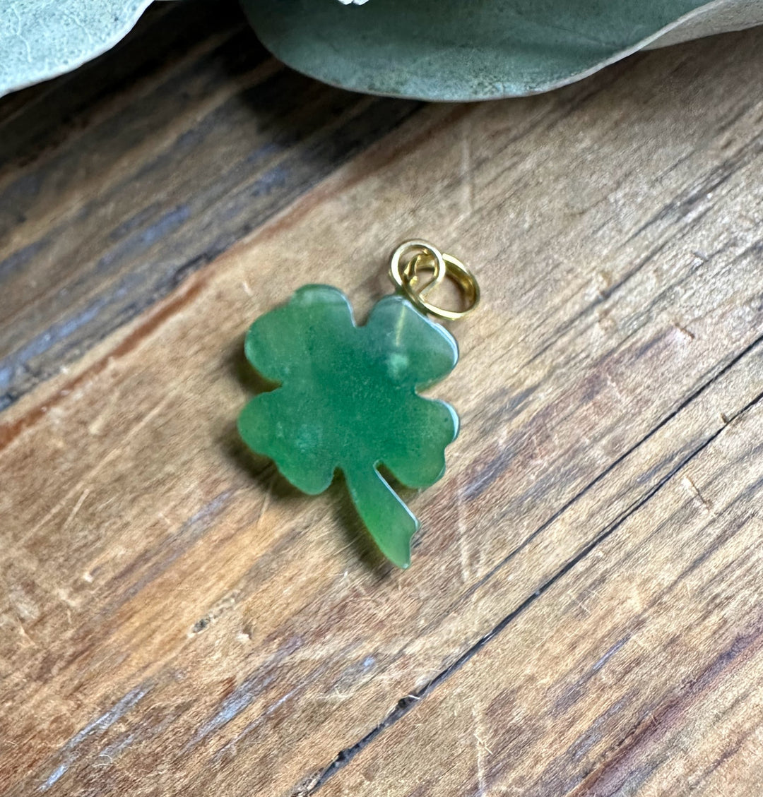 Green shamrock charm with a small gold loop for attaching to jewelry on a wooden surface
