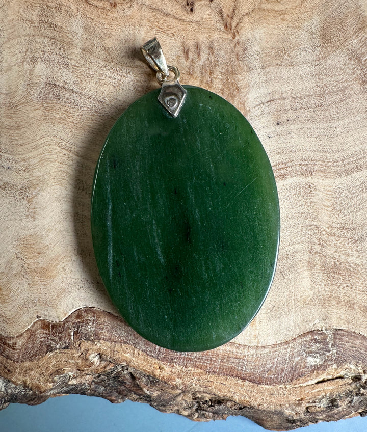 Back view of oval green jade pendant with a metal bail on a black cord necklace
