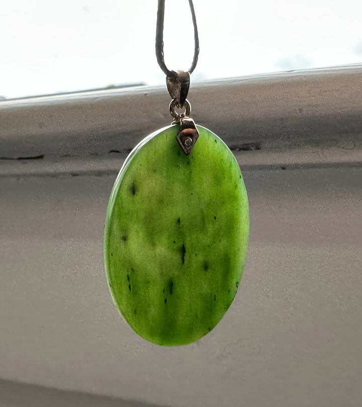 Front view of oval green jade pendant with a small metal bail on a black cord necklace