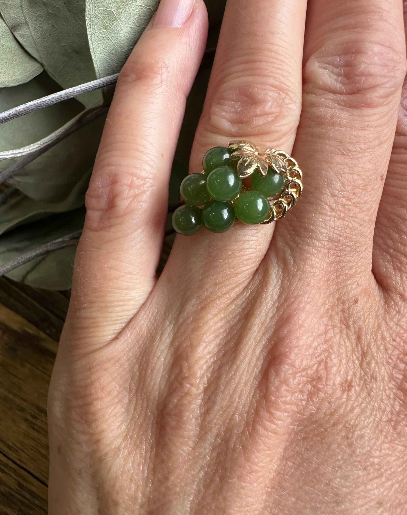 Close up of vintage Jade grape ring on finger featuring green bead cluster and gold leaf setting.