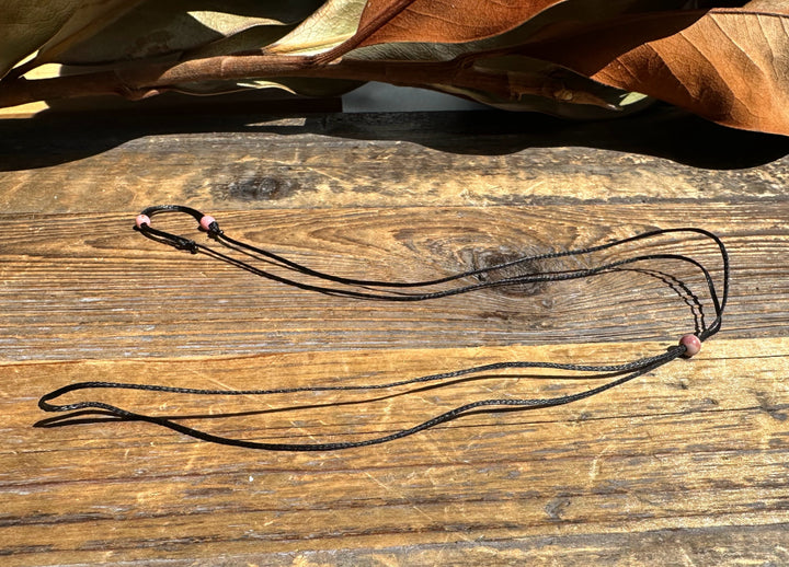 Long wax cord necklace with rhodonite beads at the ends laid across a wood surface