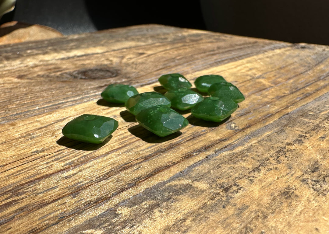 Several faceted green jade beads with holes for stringing spread on a wooden surface