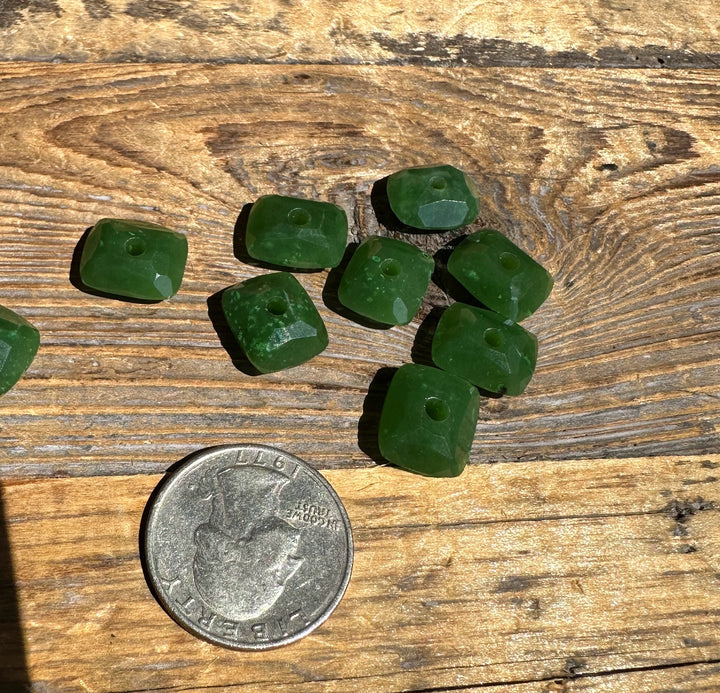 Group of square green jade beads with central holes for stringing on a wood surface with a US quarter for scale