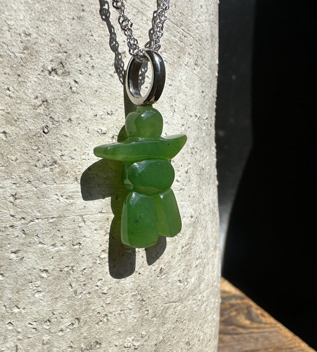 Green stone inukshuk pendant on a silver chain against a light stone background