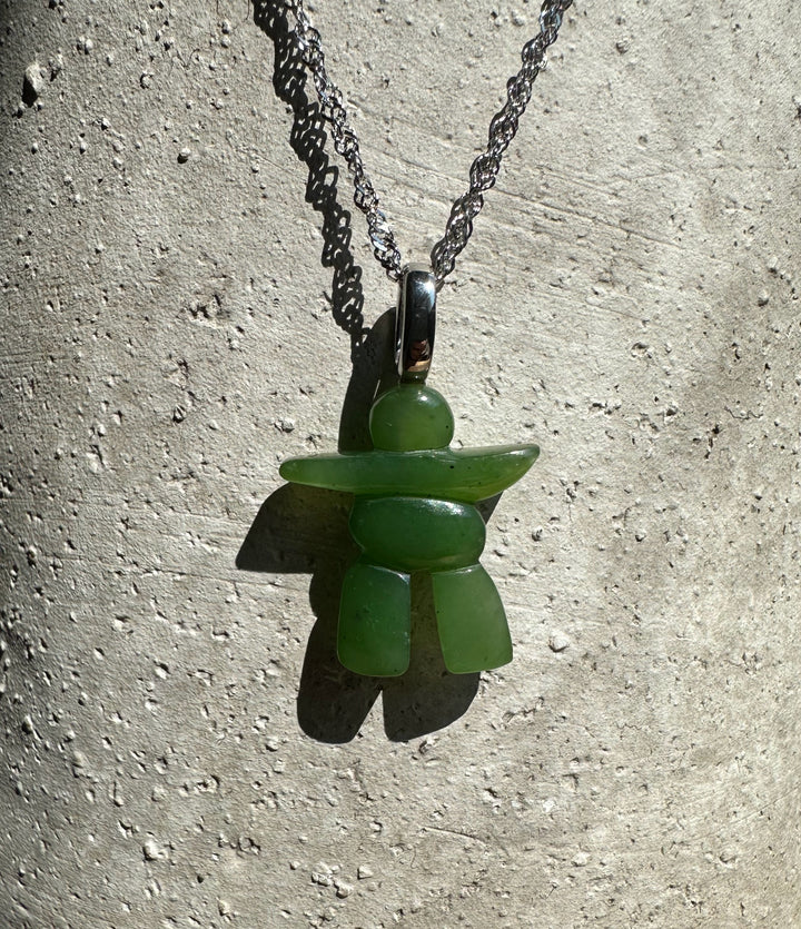Close-up of green inukshuk pendant on a silver chain against a textured concrete surface