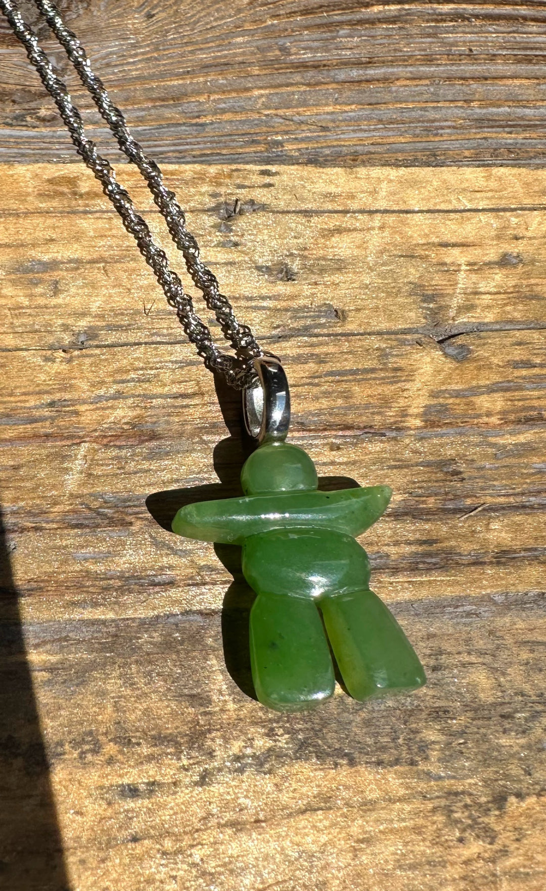 Green jade Inukshuk pendant on a silver bail with chain against a wooden surface