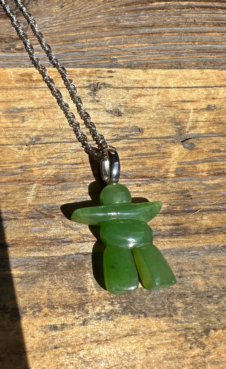 Green jade Inukshuk pendant on a silver bail with chain against a wooden surface